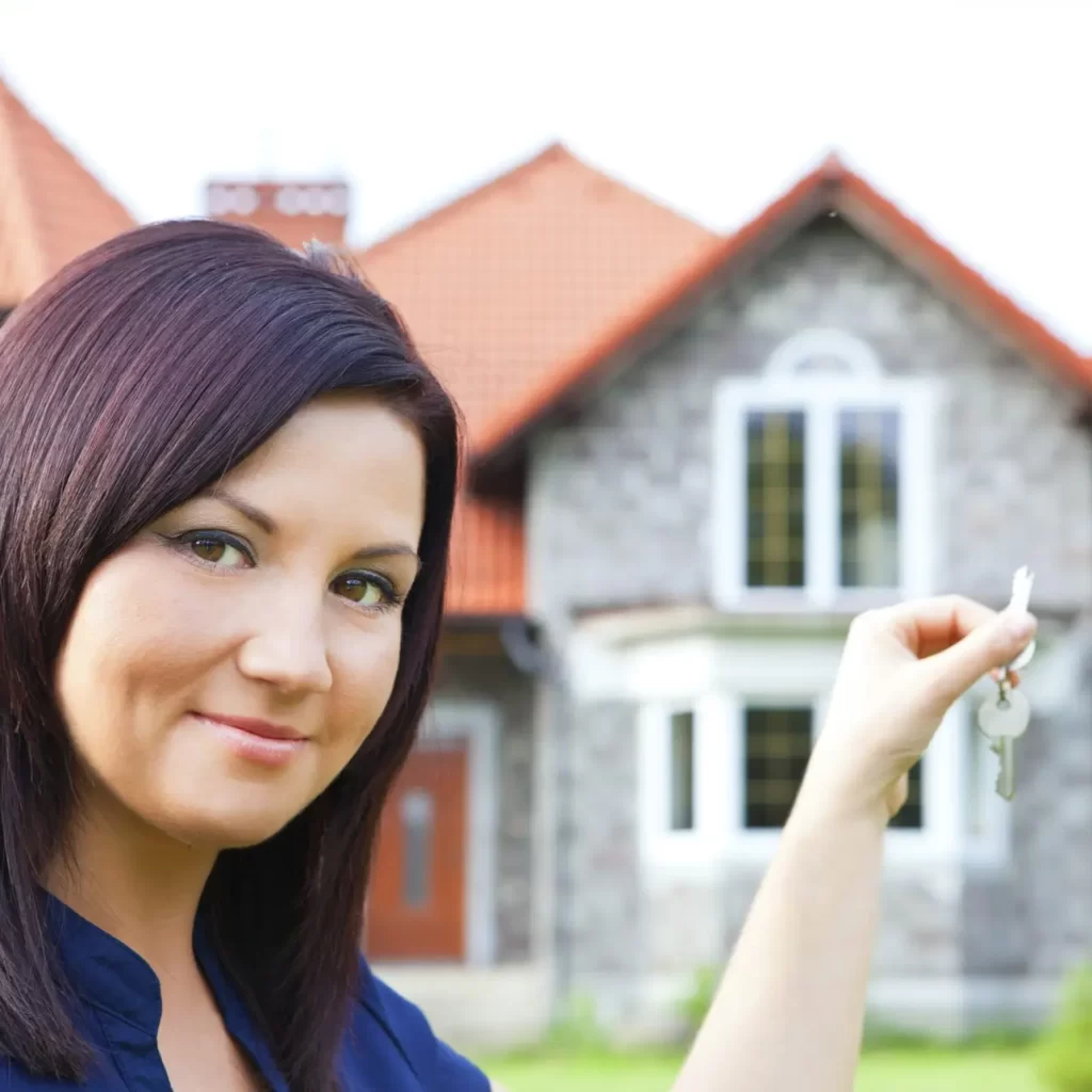 smiling woman holding keys with house in background Confident woman holding keys in front of newly sold home, symbolizing successful FSBO home sale